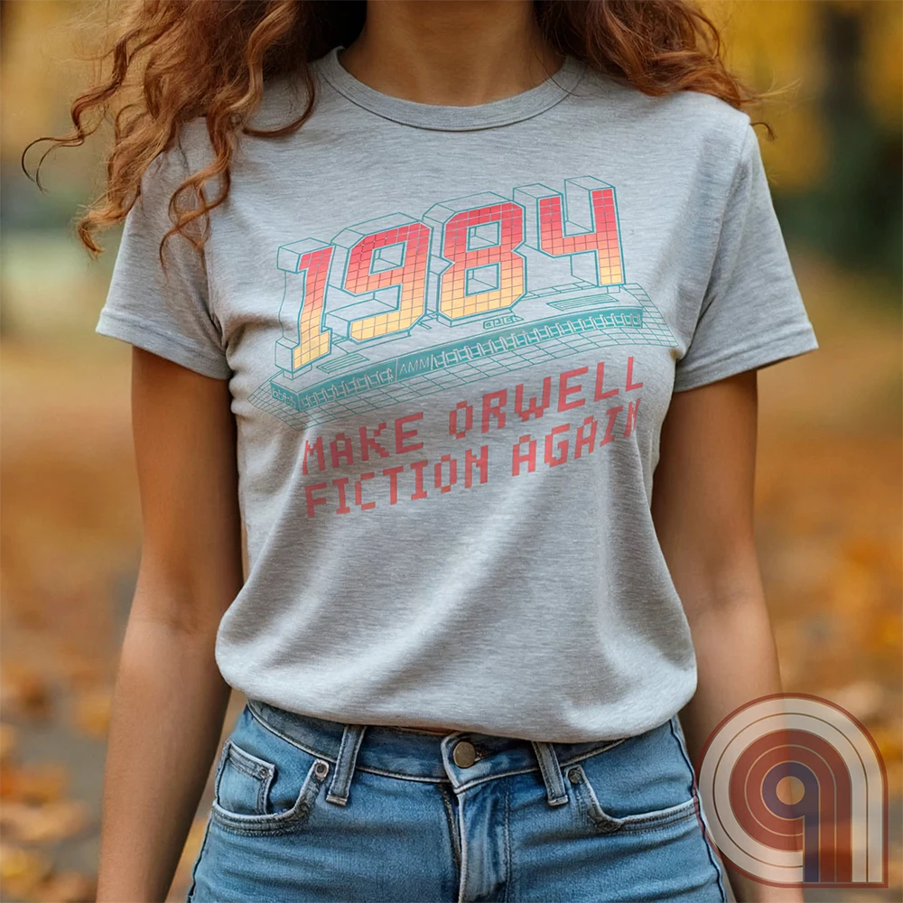 Light ash grey T-shirt tucked into jeans on a model, featuring large gradient “1984” numerals above a teal retro computer keyboard and red pixel lettering “MAKE ORWELL FICTION AGAIN”, a visual nod to Orwell's dystopian novel.