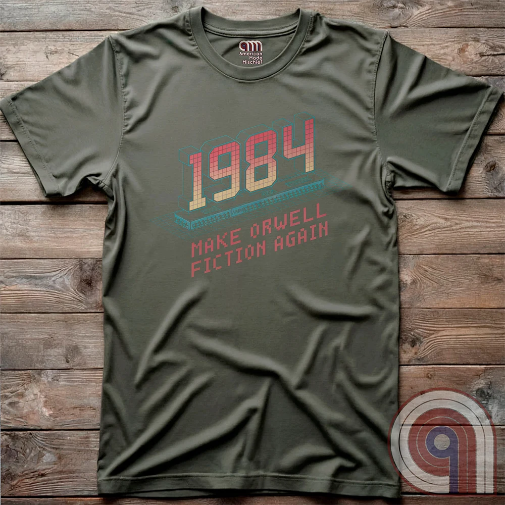 Flat-lay olive green T-shirt with a retro computer illustration below gradient “1984” numerals and the anti-Orwellian message “MAKE ORWELL FICTION AGAIN” printed in red blocky type.