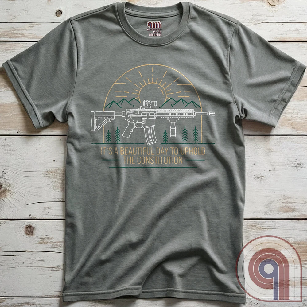 America was forged by the armed & unafraid. This ‘It’s a Beautiful Day to Uphold the Constitution’ t-shirt fuses the love of firearms with the untamed American spirit. Featuring an AR-15 set against rugged mountains and a blazing sunrise, this design screams independence, defiance, & unbreakable resolve. Whether you’re a hunter, soldier, or just a patriot who will not comply, this 2A shirt is a warning to tyrants: We don’t retreat. We reload. Wear it proudly and show that America will never bow; Color- Grey