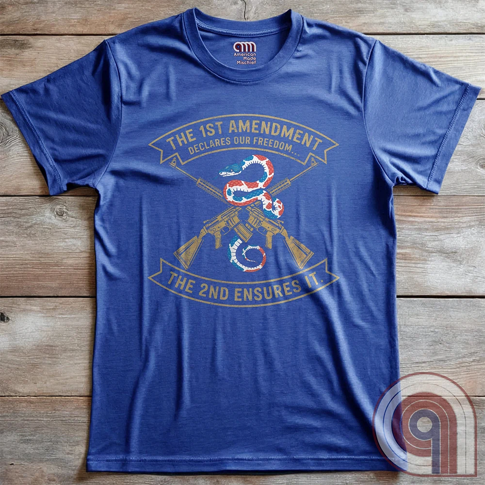 Flat-lay heather blue T-shirt with a red, white and blue snake curling above crossed golden rifles and the two banners “THE 1ST AMENDMENT DECLARES OUR FREEDOM...” and “THE 2ND ENSURES IT”.