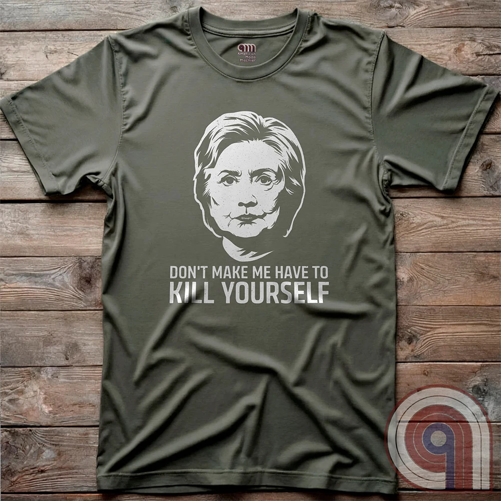 Olive green shirt displayed flat on weathered planks; the chest print is a pale political portrait over bold “KILL YOURSELF” text completing the satirical phrase.