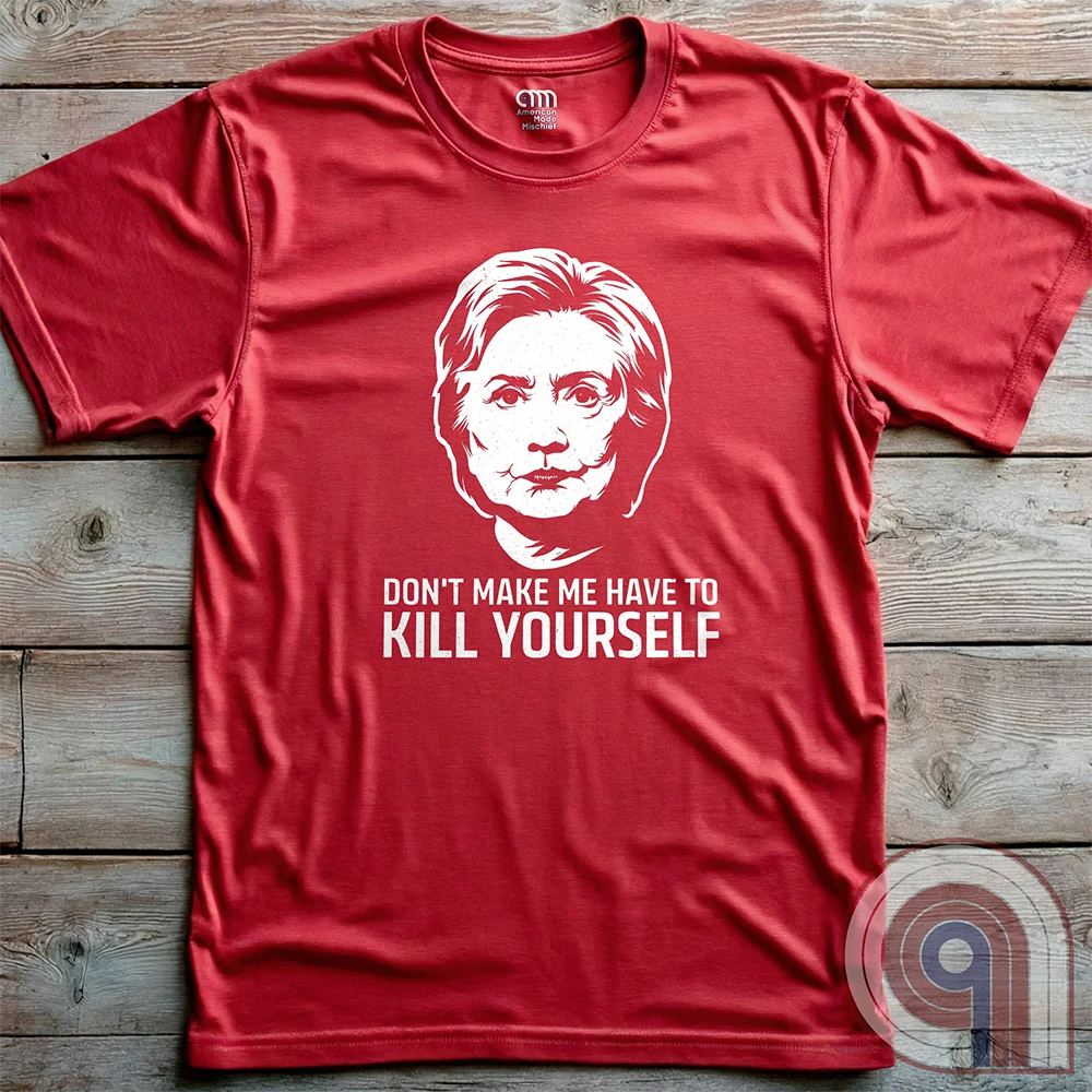 Red T-shirt photographed flat against wood, showing a high-contrast pale portrait of Hillary Clinton over the dark, conspiratorial satirical slogan “DON'T MAKE ME HAVE TO KILL YOURSELF”.