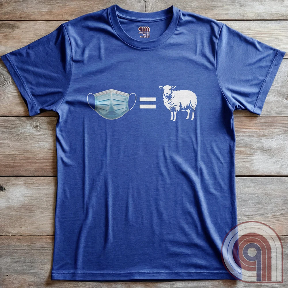Blue shirt arranged flat over rustic wood, featuring the simple mask-equals-sheep equation in blue and white with wide negative space around the graphic.