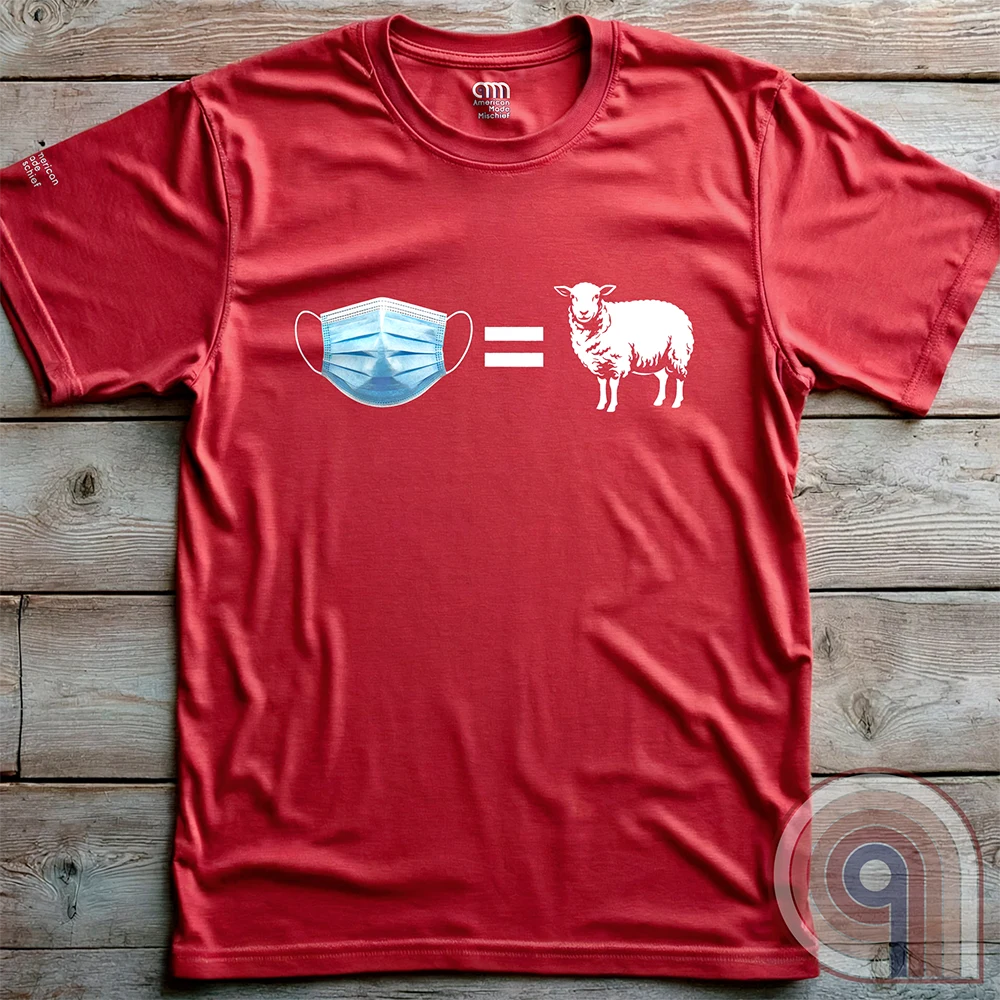 Red T-shirt shown flat on wooden boards, its simple blue, white and grey artwork forming the equation of a disposable face mask and a sheep.