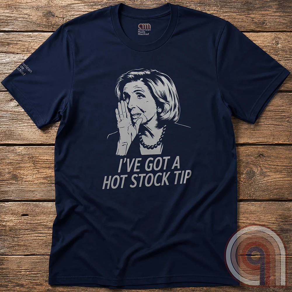 A navy T-shirt photographed flat on wood, its pale portrait and stock-tip slogan forming a simple black-and-white-style political satire.