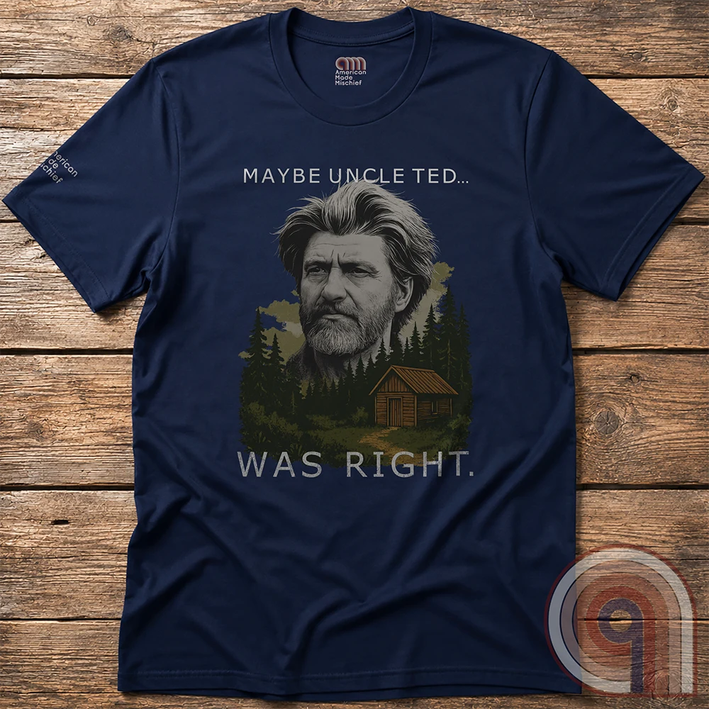 A navy tee laid flat on wooden boards, showing a rugged bearded portrait, evergreen forest and cabin beneath the sardonic slogan “MAYBE UNCLE TED... WAS RIGHT.”