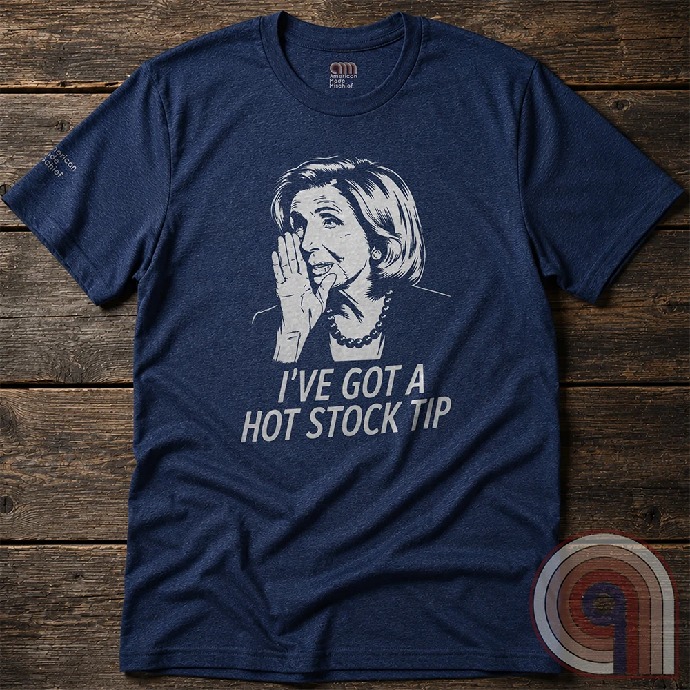 Heather navy T-shirt spread over dark wooden boards, featuring a light-colored whispering portrait and an insider-trading satire captioned “I’VE GOT A HOT STOCK TIP”.