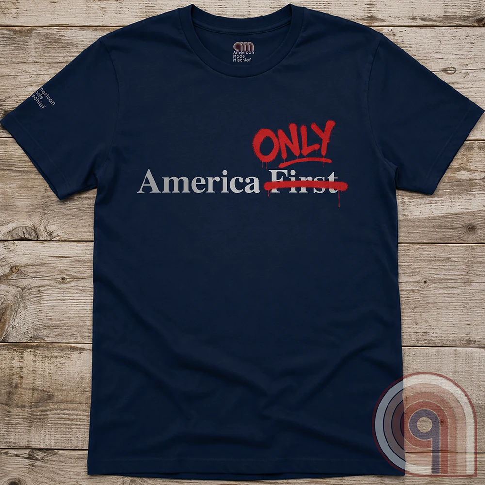 Navy crewneck laid flat on wood, showing the hand-corrected slogan “America First”: “First” struck through and red “ONLY” above.