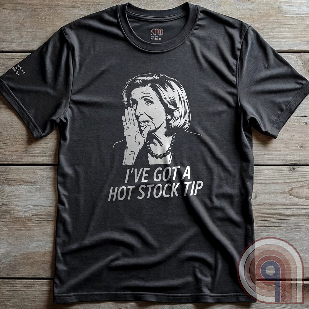 Charcoal T-shirt laid flat on wooden boards, showing the whispering-woman graphic in light ink with the same bold “I’VE GOT A HOT STOCK TIP” caption.