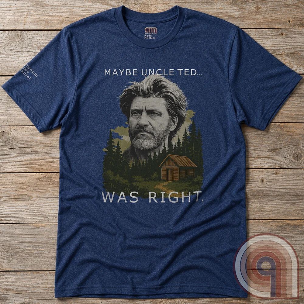 A heather navy shirt photographed flat on wood, featuring a grayscale man’s face floating over pine trees and a cabin, between “MAYBE UNCLE TED...” and “WAS RIGHT.”