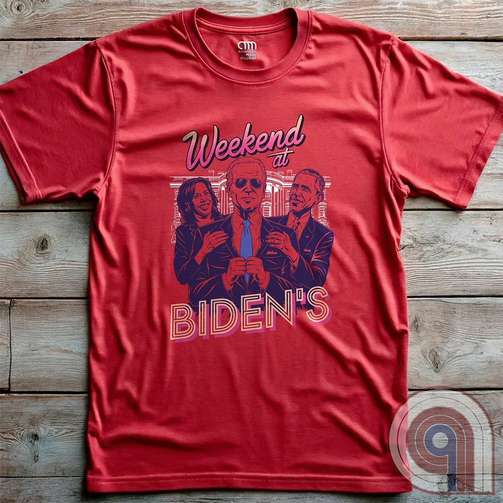 Red T-shirt laid flat, displaying the complete “Weekend at BIDEN’S” retro movie parody: Joe Biden in sunglasses between Kamala Harris and Barack Obama, with purple illustration and pink headline lettering.